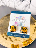A pair of square stud earrings with an brown and black tiger-stripe pattern, mounted on a white display card with blue borders. The card is branded 'BEST & CO.