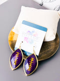 Purple football-shaped drop earrings with gold trim and yellow lacing details, displayed on a white card with the brand name Best & Co. on a gold tray with a white cushion.