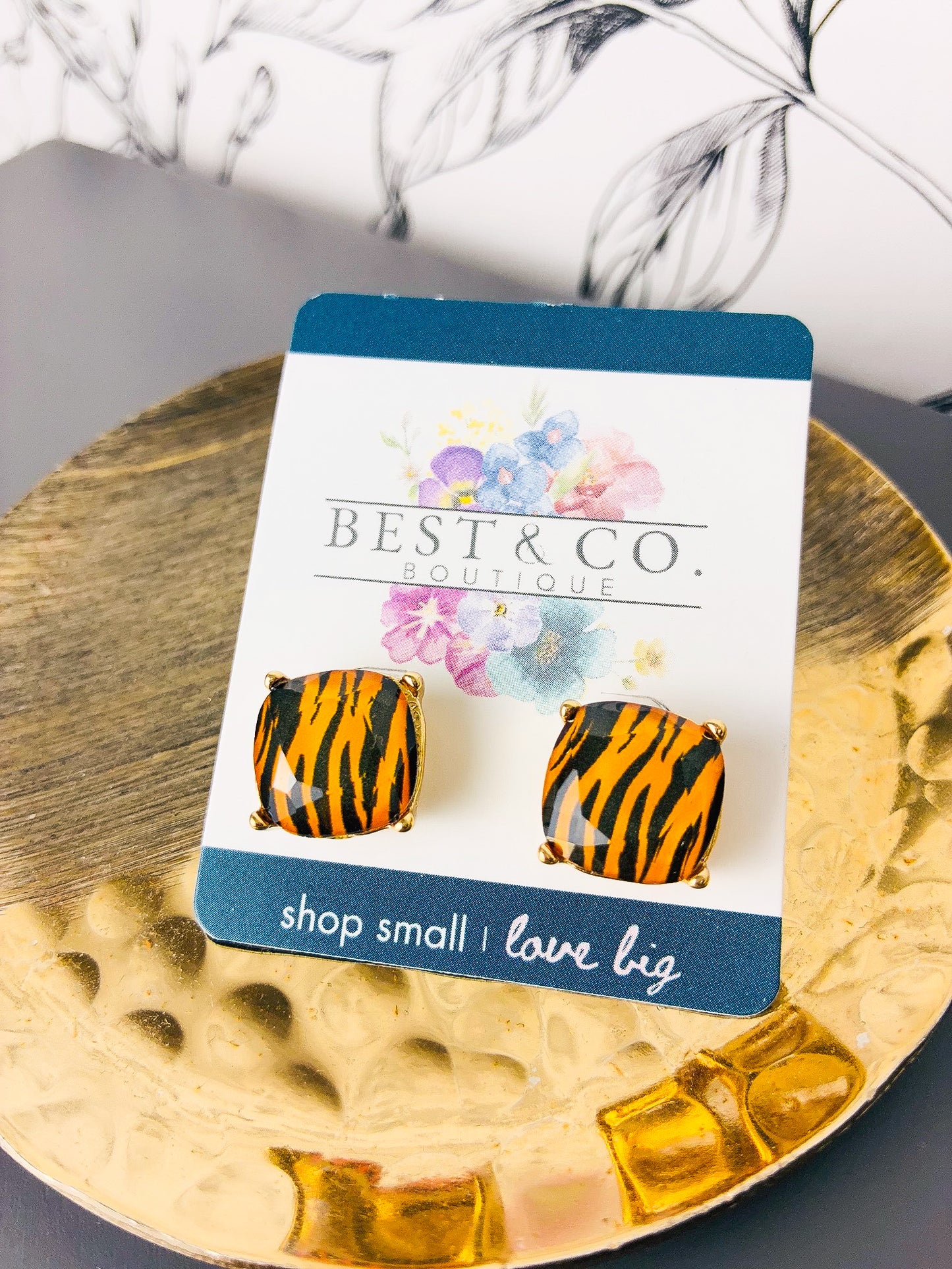 A pair of square stud earrings with an brown and black tiger-stripe pattern, mounted on a white display card with blue borders. The card is branded 'BEST & CO.